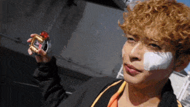 a man with curly hair and a bandage on his face is holding a device