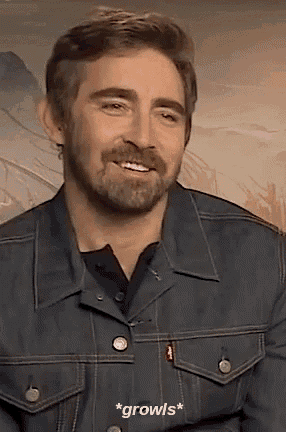 a man with a beard wearing a denim jacket is smiling and talking .