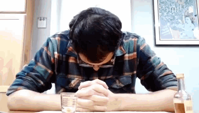 a man in a plaid shirt sits at a table with his head down