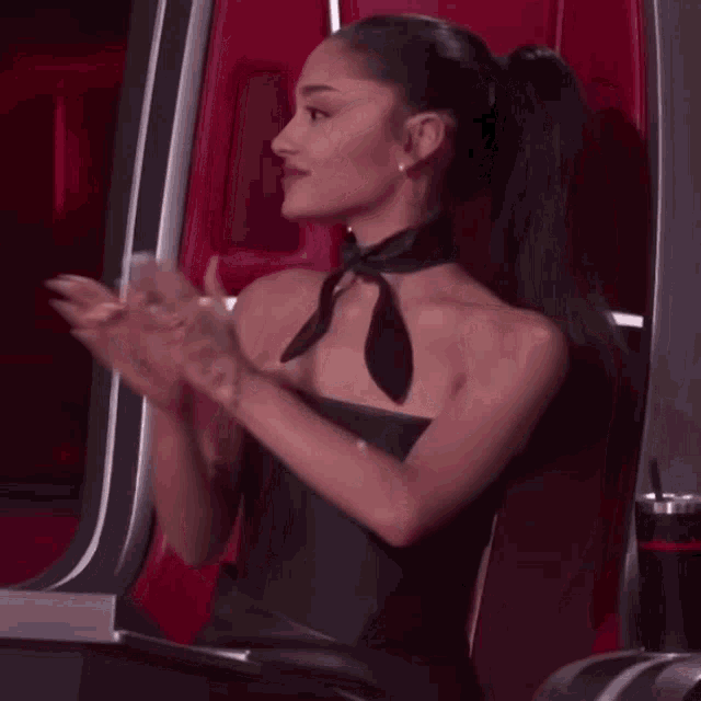ariana grande is wearing a black strapless dress and a black scarf around her neck .