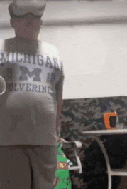 a man wearing a michigan wolverines shirt is standing in a room