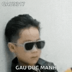 a young boy wearing sunglasses is leaning against a wall and making a funny face .