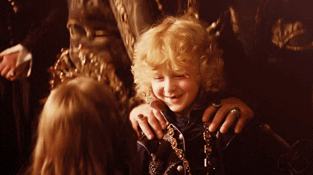 a little boy with blonde curly hair is smiling while being held by a woman