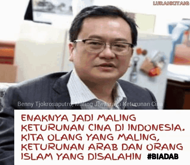 a man wearing glasses and a suit is behind a sign that says " enaknya jadi maling keturunan cina di indonesia "