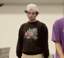 a man wearing a white hat and a black sweater is standing next to another man wearing a purple shirt .