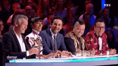 a group of people are sitting at a table in front of a crowd watching a show .