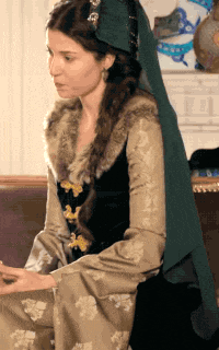 a woman wearing a black and gold dress with a fur collar sits on a couch