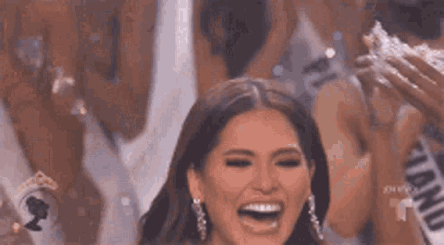 a woman is smiling and holding a crown in her hand while standing in front of a crowd .