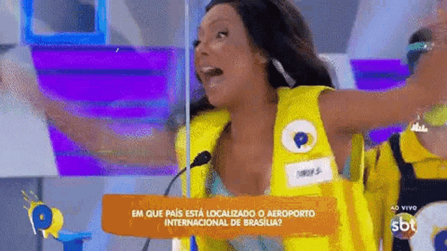 a woman in a yellow vest is standing in front of a microphone with her arms in the air .