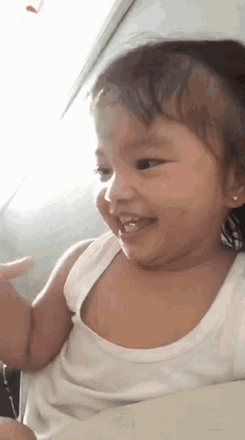 a little girl in a white tank top is smiling .