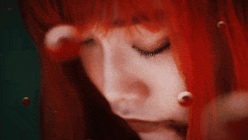 a close up of a woman 's face with red hair and a green background
