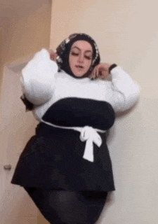 a woman wearing a hijab and a white top is standing in a room .