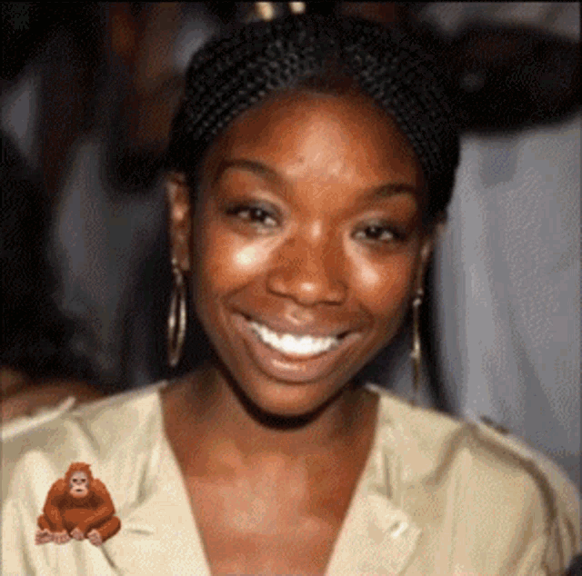 a woman with braids and hoop earrings smiles with a picture of an orangutan in the corner