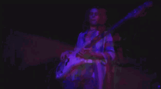 a person is playing a guitar in a dark room with purple lights .