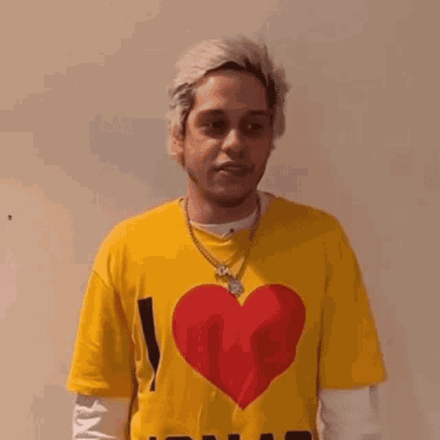 a young man is wearing a yellow t-shirt with a red heart on it .
