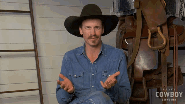 a man wearing a cowboy hat is sitting in front of a saddle and a sign that says ultimate cowboy showdown