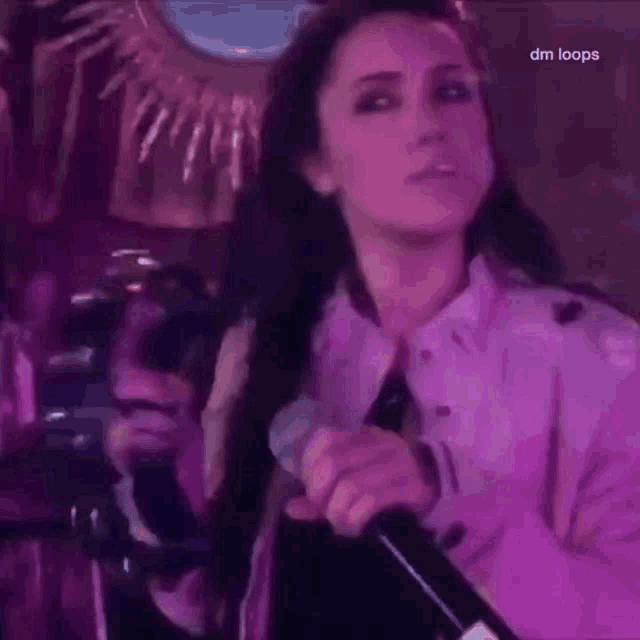 a woman is singing into a microphone while wearing a purple jacket .