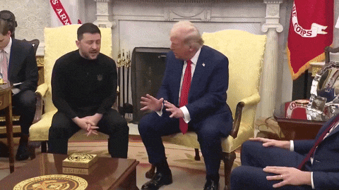 a man in a suit sits next to a man in a black shirt and a man in a red tie