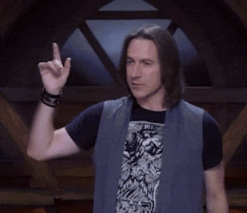 a man wearing a vest and a black shirt is pointing upwards