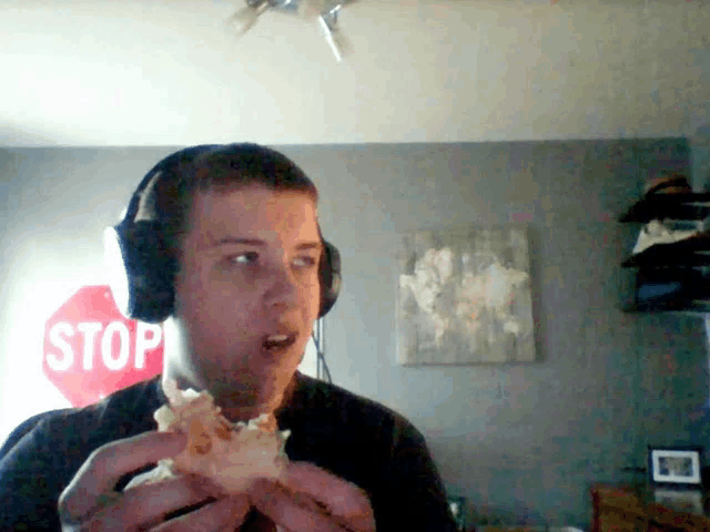 a man wearing headphones is eating a piece of pizza in front of a stop sign