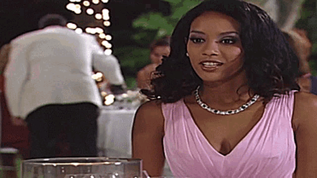 a woman in a pink dress is sitting at a table with a glass