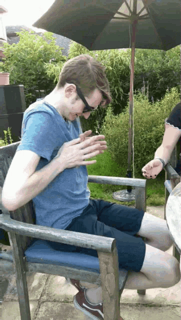 a man in a blue shirt is sitting in a chair with his hands folded