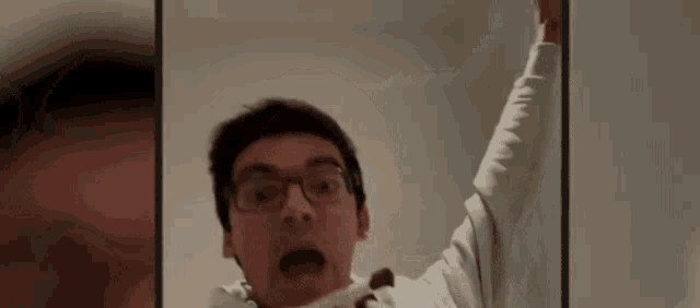 a man wearing glasses is making a funny face while holding his arm up .