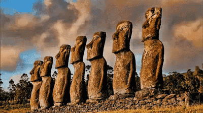 a row of stone statues in a field with trees in the background