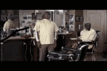 a man in a yellow shirt is standing next to a man in a barber chair