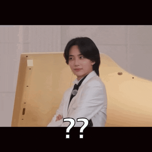 a man in a tuxedo is standing in front of a piano and has a question mark on his face .