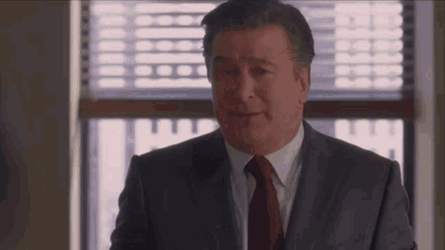 a man in a suit and red tie is standing in front of a window .