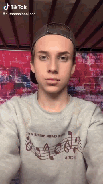 a young man wearing a grey shirt with music notes on it and a hat