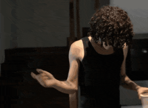 a man with curly hair is standing in a dark room holding a cup
