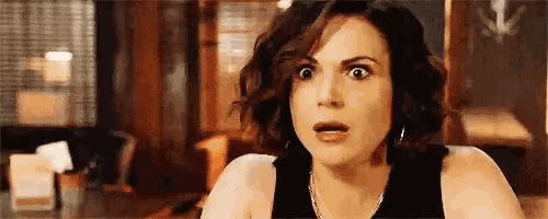 a woman with short hair is making a surprised face while sitting at a table .