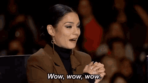 a woman is sitting in a chair in front of a crowd and saying wow .