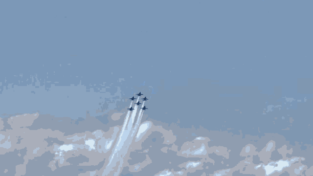 a group of fighter jets flying through a blue sky with smoke trails