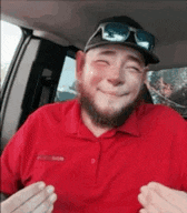 a man with a beard wearing a red shirt and sunglasses is sitting in a car .