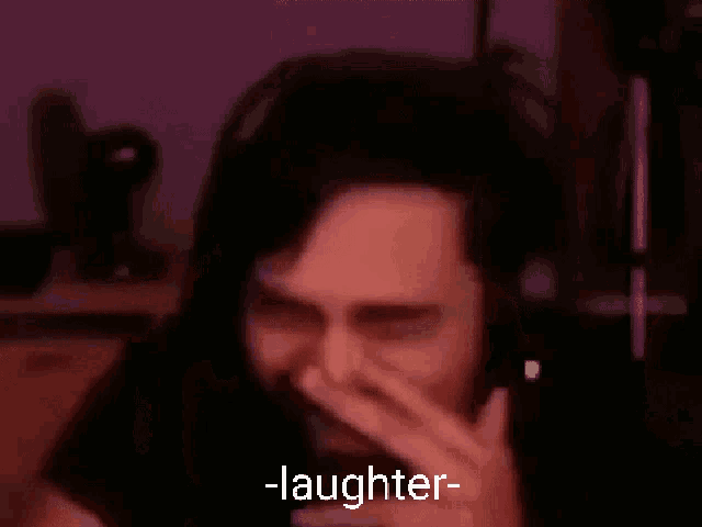 a man with headphones is laughing with his hand over his mouth .