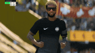 a man wearing sunglasses and a black nike shirt is running on a sports field