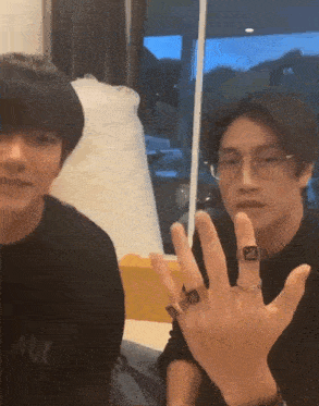 a man wearing glasses and a ring on his finger is sitting next to another man .