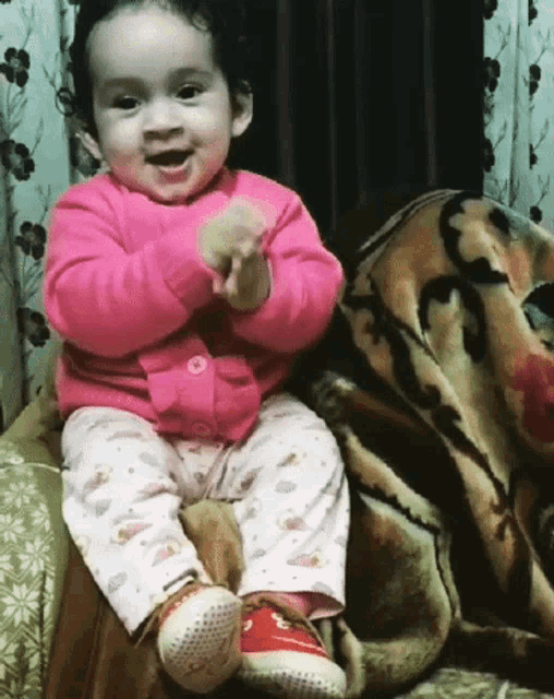a little girl in a pink sweater and pink pants is sitting on a couch