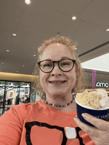 a woman is holding a cup of ice cream in front of an amc building