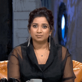a woman in a black jacket and earrings is sitting in a chair and making a funny face .