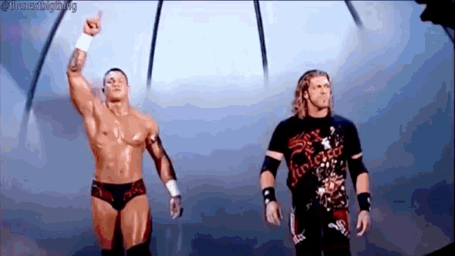 two wrestlers are standing next to each other in a ring and one is pointing up .
