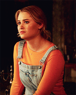 a young woman wearing overalls and an orange shirt