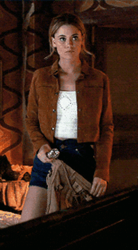 a woman wearing shorts and a brown jacket is standing in a room