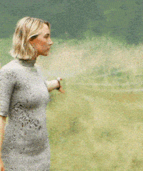 a woman in a grey dress is standing in a field with her hand on her head