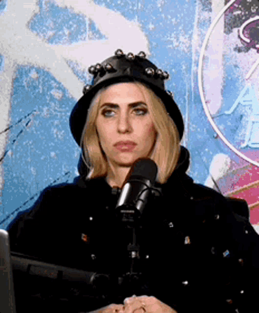a woman wearing a hat is sitting in front of a microphone in front of a neon sign that says ae