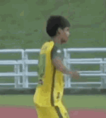 a young boy in a yellow and green soccer uniform is walking on a field .