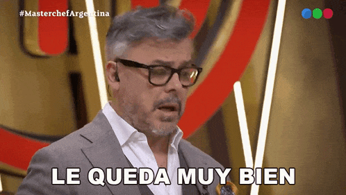 a man wearing glasses and a suit says " le queda muy bien "